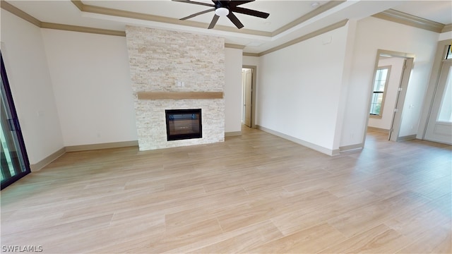 unfurnished living room featuring light hardwood / wood-style flooring, a raised ceiling, a stone fireplace, and ceiling fan