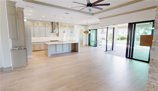 kitchen with decorative light fixtures, light stone countertops, ceiling fan, light hardwood / wood-style flooring, and a kitchen island with sink