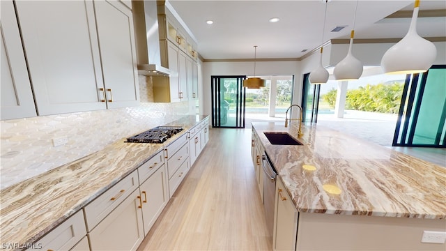 kitchen featuring decorative light fixtures, backsplash, a kitchen island with sink, sink, and wall chimney range hood