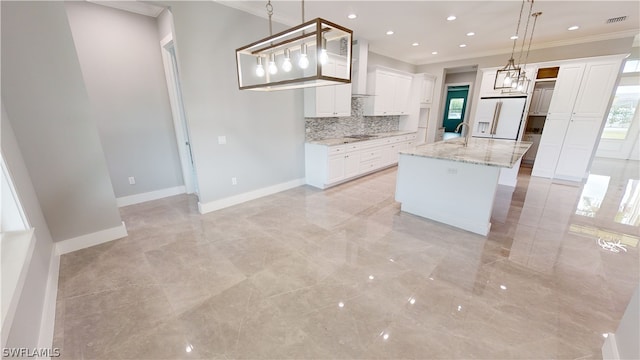 kitchen featuring white fridge with ice dispenser, a center island with sink, light stone countertops, wall chimney exhaust hood, and decorative light fixtures