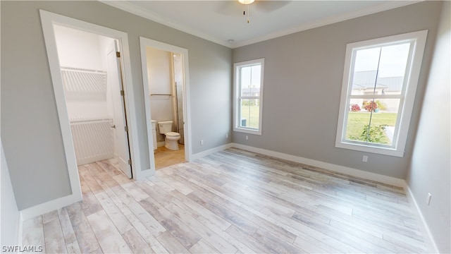 unfurnished bedroom featuring a closet, ensuite bath, light hardwood / wood-style floors, ornamental molding, and a spacious closet