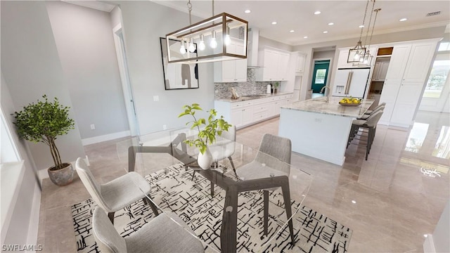 kitchen with white refrigerator with ice dispenser, an island with sink, light stone counters, wall chimney range hood, and decorative light fixtures