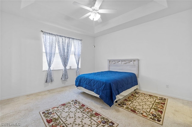 carpeted bedroom with a raised ceiling and ceiling fan