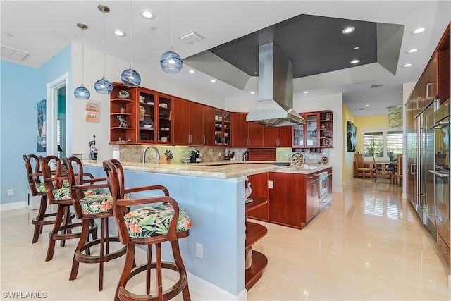 kitchen featuring light stone countertops, pendant lighting, island exhaust hood, kitchen peninsula, and decorative backsplash