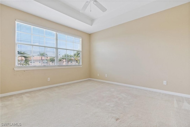 unfurnished room with ceiling fan, a tray ceiling, and light carpet