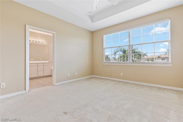 unfurnished bedroom with a raised ceiling, ceiling fan, light colored carpet, and ensuite bath