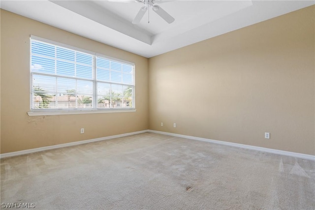 spare room with a raised ceiling, light carpet, and ceiling fan