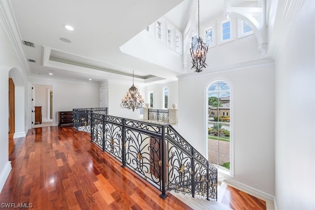 hall featuring a raised ceiling, ornamental molding, a notable chandelier, and dark wood-type flooring