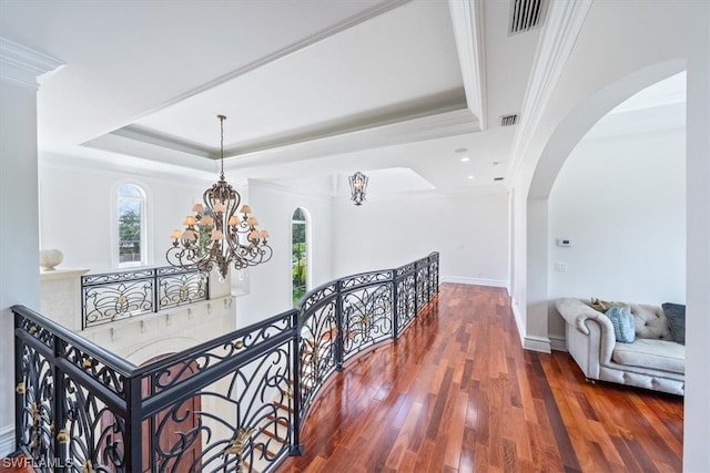 hall featuring crown molding, a tray ceiling, dark wood-type flooring, and an inviting chandelier