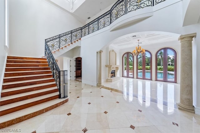 tiled entrance foyer featuring a towering ceiling, crown molding, coffered ceiling, ornate columns, and an inviting chandelier