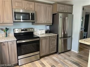 kitchen featuring appliances with stainless steel finishes, light hardwood / wood-style flooring, and light stone countertops