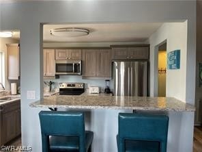 kitchen with appliances with stainless steel finishes, sink, a breakfast bar, and light stone counters