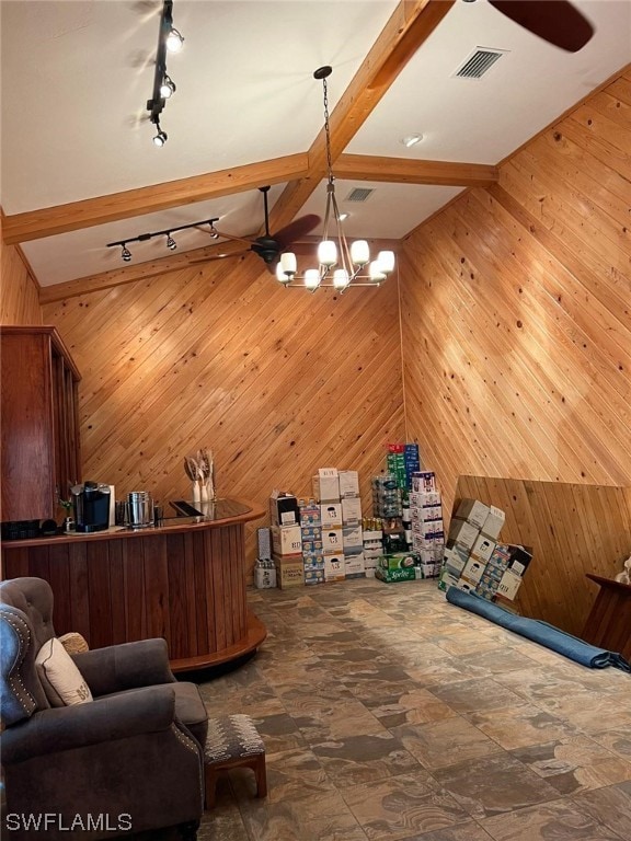 interior space featuring dark tile flooring, lofted ceiling with beams, wood walls, track lighting, and an inviting chandelier