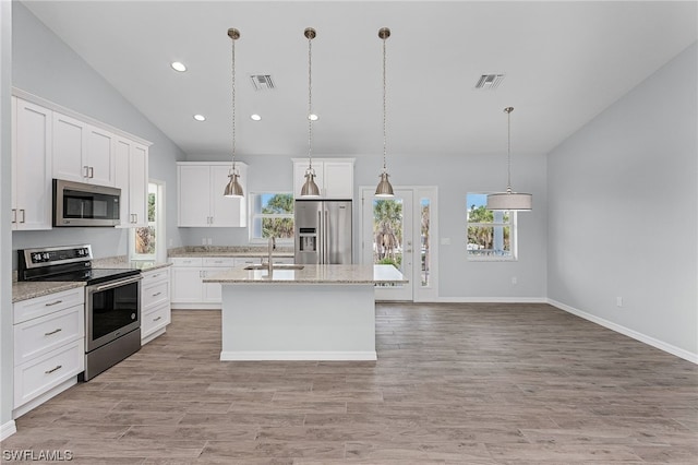 kitchen with lofted ceiling, white cabinets, hanging light fixtures, an island with sink, and stainless steel appliances