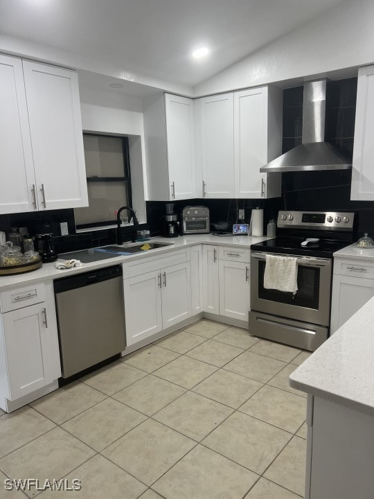 kitchen with wall chimney range hood, lofted ceiling, stainless steel appliances, and white cabinetry