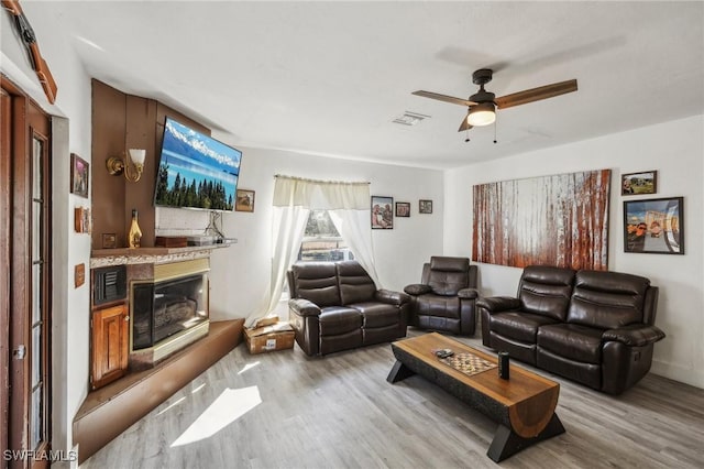 living room with ceiling fan, a fireplace, and light hardwood / wood-style flooring