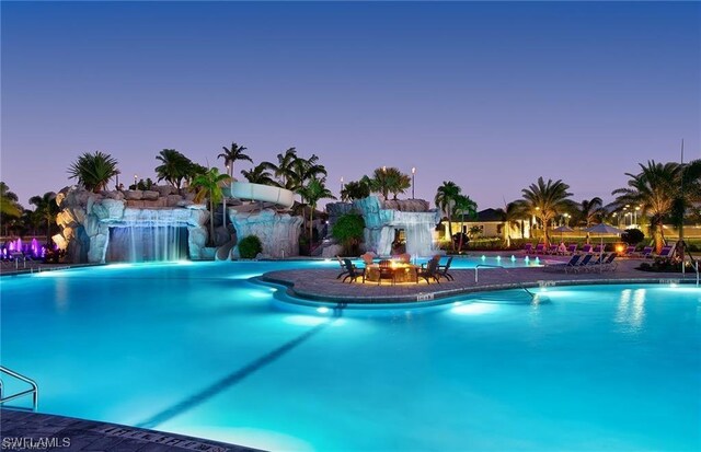 pool at dusk featuring a water slide and pool water feature