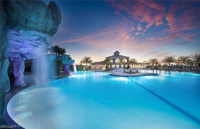 pool at dusk featuring pool water feature and a gazebo