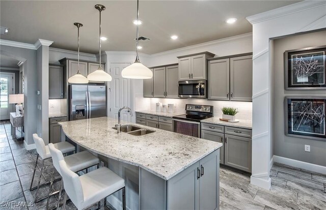 kitchen with sink, pendant lighting, backsplash, stainless steel appliances, and a center island with sink