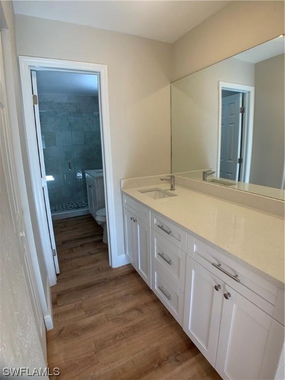 bathroom with toilet, vanity, a shower with shower door, and hardwood / wood-style flooring