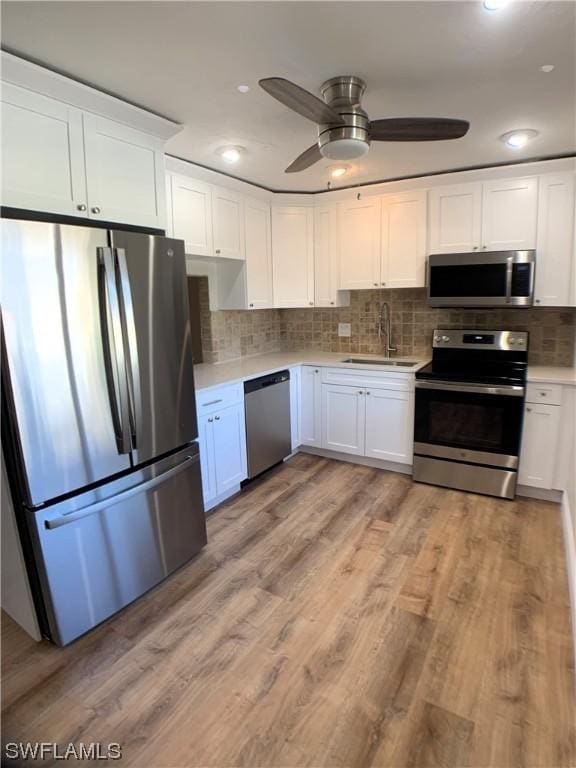 kitchen featuring tasteful backsplash, stainless steel appliances, sink, light hardwood / wood-style flooring, and white cabinets