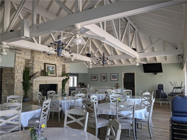 dining room with beam ceiling, wood-type flooring, a fireplace, and high vaulted ceiling