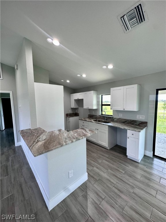 kitchen featuring light stone counters, white cabinetry, and sink