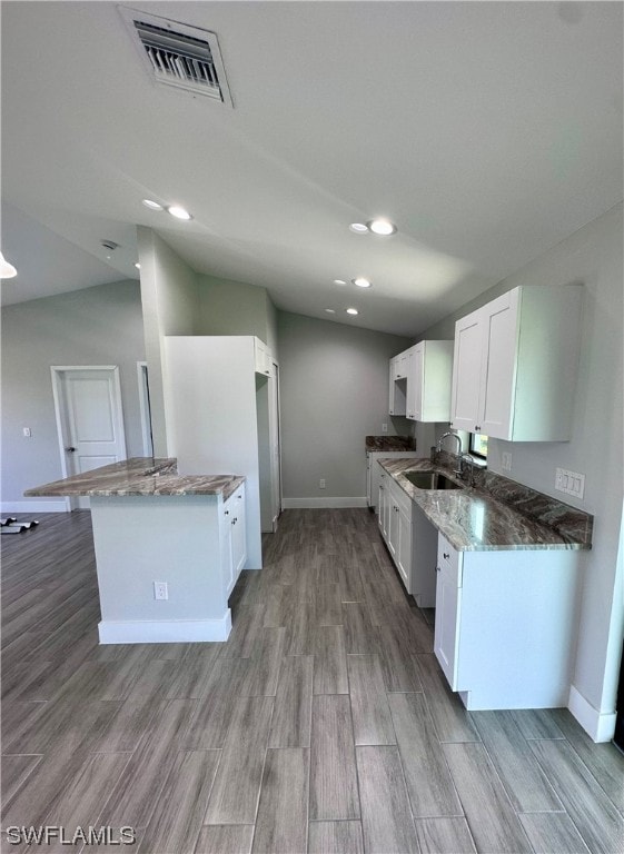 kitchen with sink, dark stone countertops, white cabinets, light hardwood / wood-style floors, and lofted ceiling