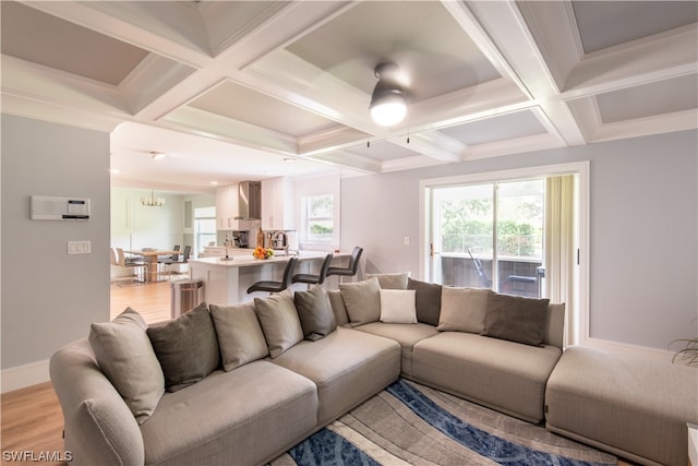 living room featuring crown molding, light hardwood / wood-style flooring, coffered ceiling, beam ceiling, and ceiling fan with notable chandelier