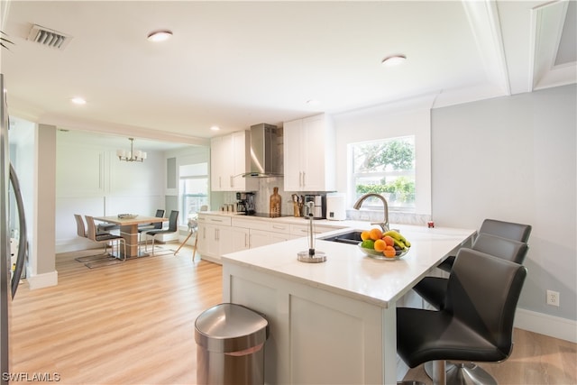 kitchen featuring light hardwood / wood-style floors, a breakfast bar area, wall chimney exhaust hood, white cabinets, and sink