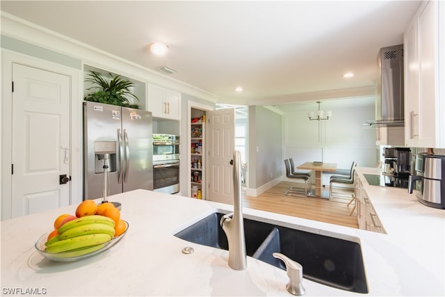 kitchen with hardwood / wood-style floors, white cabinets, appliances with stainless steel finishes, wall chimney range hood, and a notable chandelier