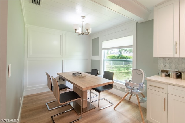 dining area with ornamental molding, a notable chandelier, and light hardwood / wood-style flooring