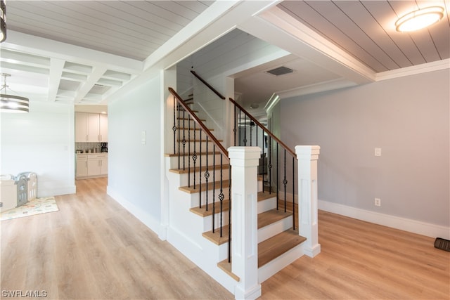 stairway with light hardwood / wood-style floors, ornamental molding, and beamed ceiling