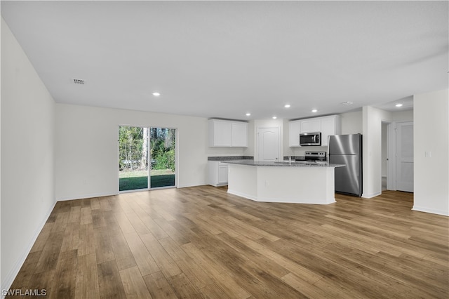 kitchen with light hardwood / wood-style floors, stainless steel appliances, white cabinets, and a center island with sink