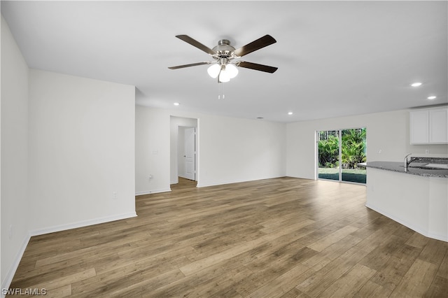 unfurnished living room with ceiling fan, sink, and light wood-type flooring