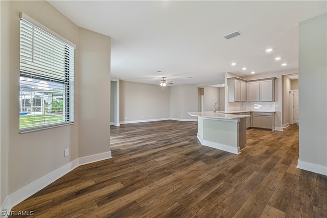 kitchen featuring an island with sink, ceiling fan, tasteful backsplash, gray cabinetry, and dark hardwood / wood-style flooring