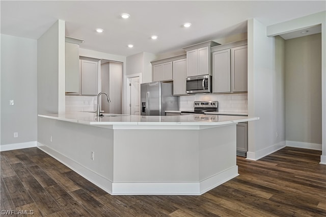 kitchen with appliances with stainless steel finishes, dark hardwood / wood-style flooring, gray cabinetry, backsplash, and sink