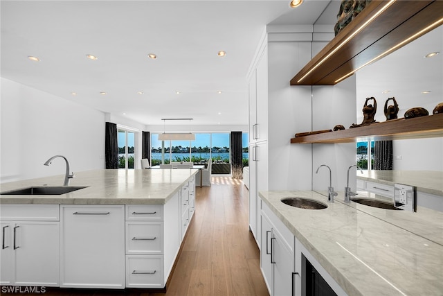 kitchen with white cabinets, light hardwood / wood-style flooring, sink, and light stone countertops