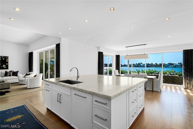 kitchen featuring white cabinets, light wood-type flooring, a kitchen island with sink, and sink