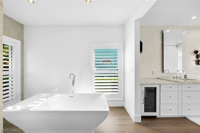 bathroom with hardwood / wood-style flooring, backsplash, beverage cooler, vanity, and a bathing tub