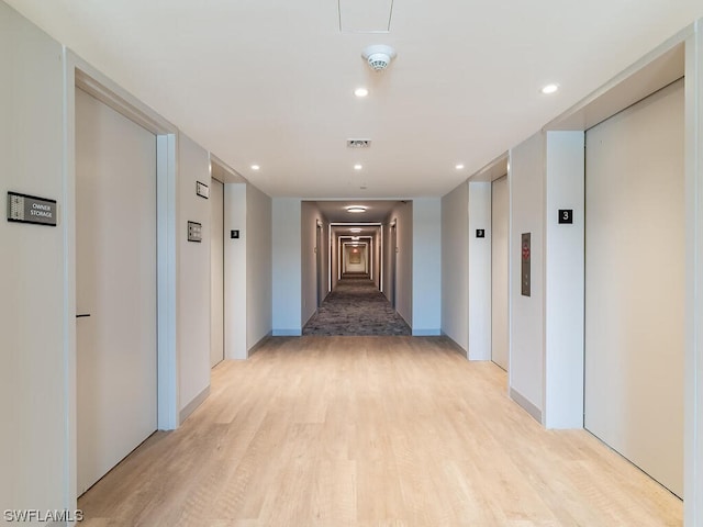 hallway with elevator and light wood-type flooring