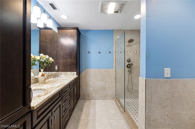 bathroom featuring tile patterned floors, vanity, a tile shower, and tile walls