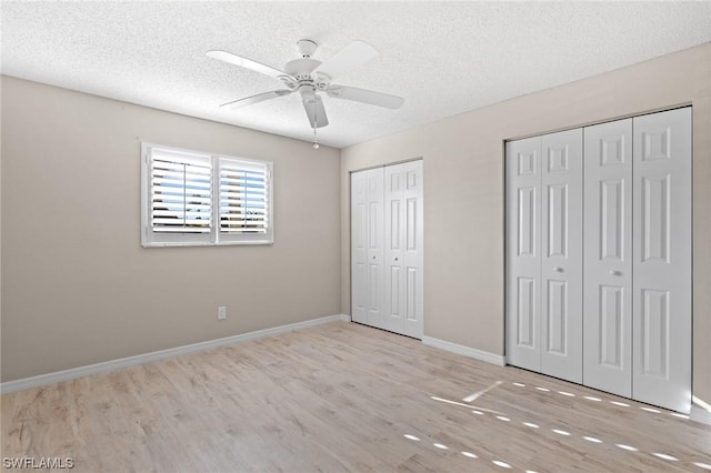 unfurnished bedroom with ceiling fan, light wood-type flooring, a textured ceiling, and two closets