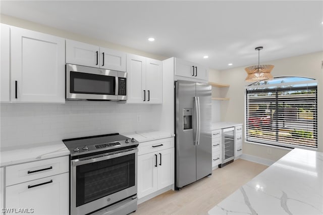 kitchen with white cabinets, appliances with stainless steel finishes, light hardwood / wood-style floors, light stone countertops, and tasteful backsplash