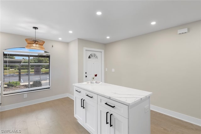 interior space with light hardwood / wood-style floors, decorative light fixtures, a center island, light stone countertops, and white cabinets