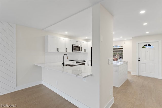 kitchen with stainless steel appliances, white cabinets, light stone countertops, and light hardwood / wood-style flooring