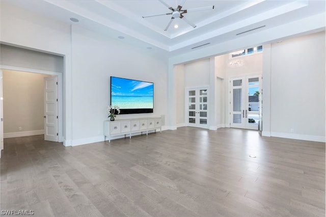 unfurnished living room featuring french doors, ceiling fan, a tray ceiling, and light wood-type flooring