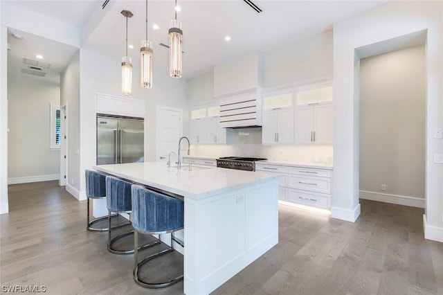 kitchen featuring high end appliances, an island with sink, decorative light fixtures, and light wood-type flooring