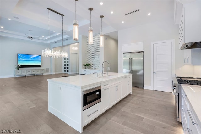 kitchen with built in appliances, pendant lighting, a raised ceiling, and light wood-type flooring