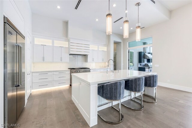 kitchen featuring decorative light fixtures, a kitchen island with sink, light hardwood / wood-style floors, a breakfast bar area, and high quality appliances